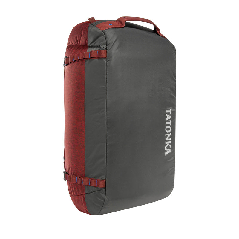 Front three-quarter view of sixty-five litre Tatonka Duffle Bag with grab handle on top and compression straps on the side - Black/Tango Red