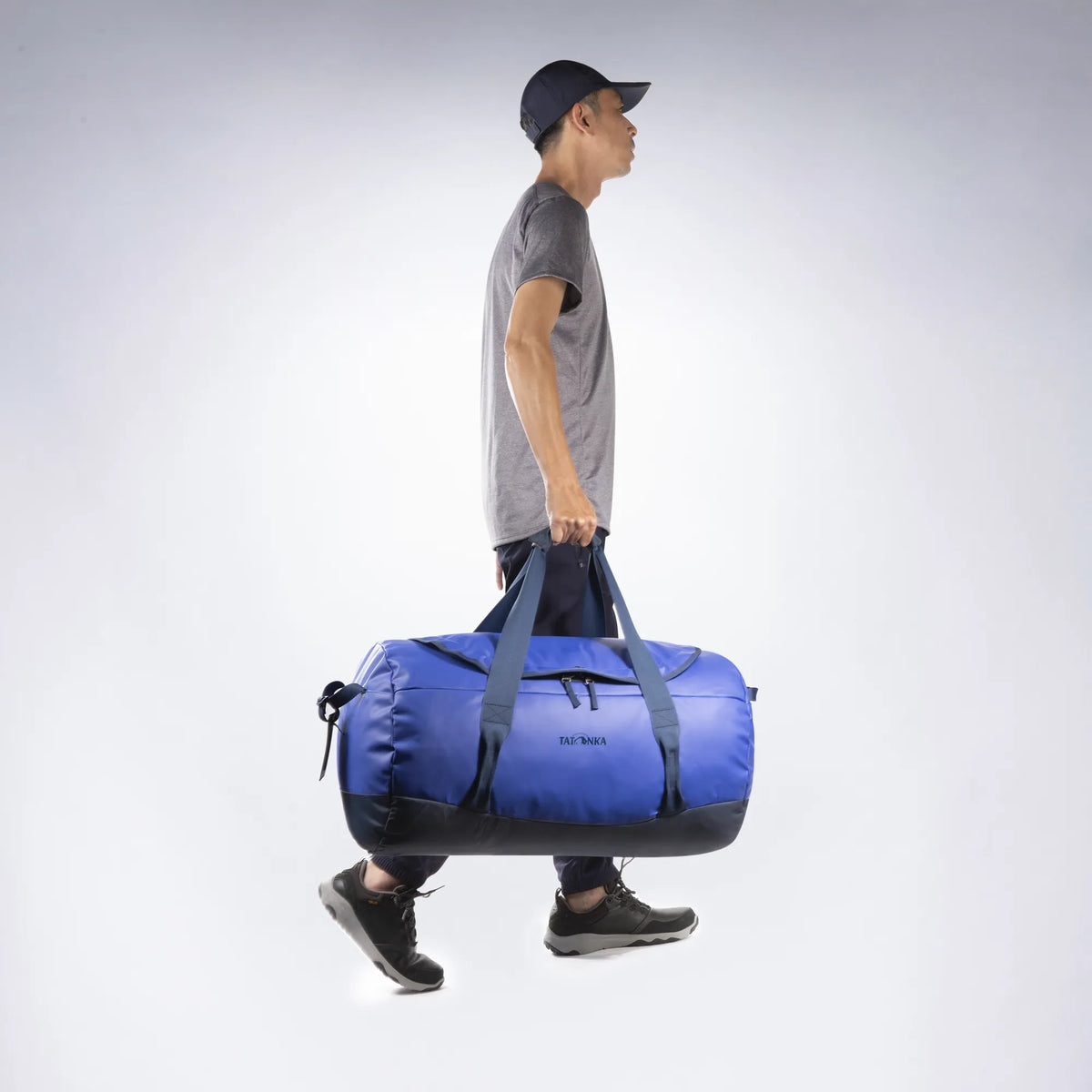 Being carried by the handles of the Tatonka Basic Barrel 65 L in matte blue | TADI.6981.410